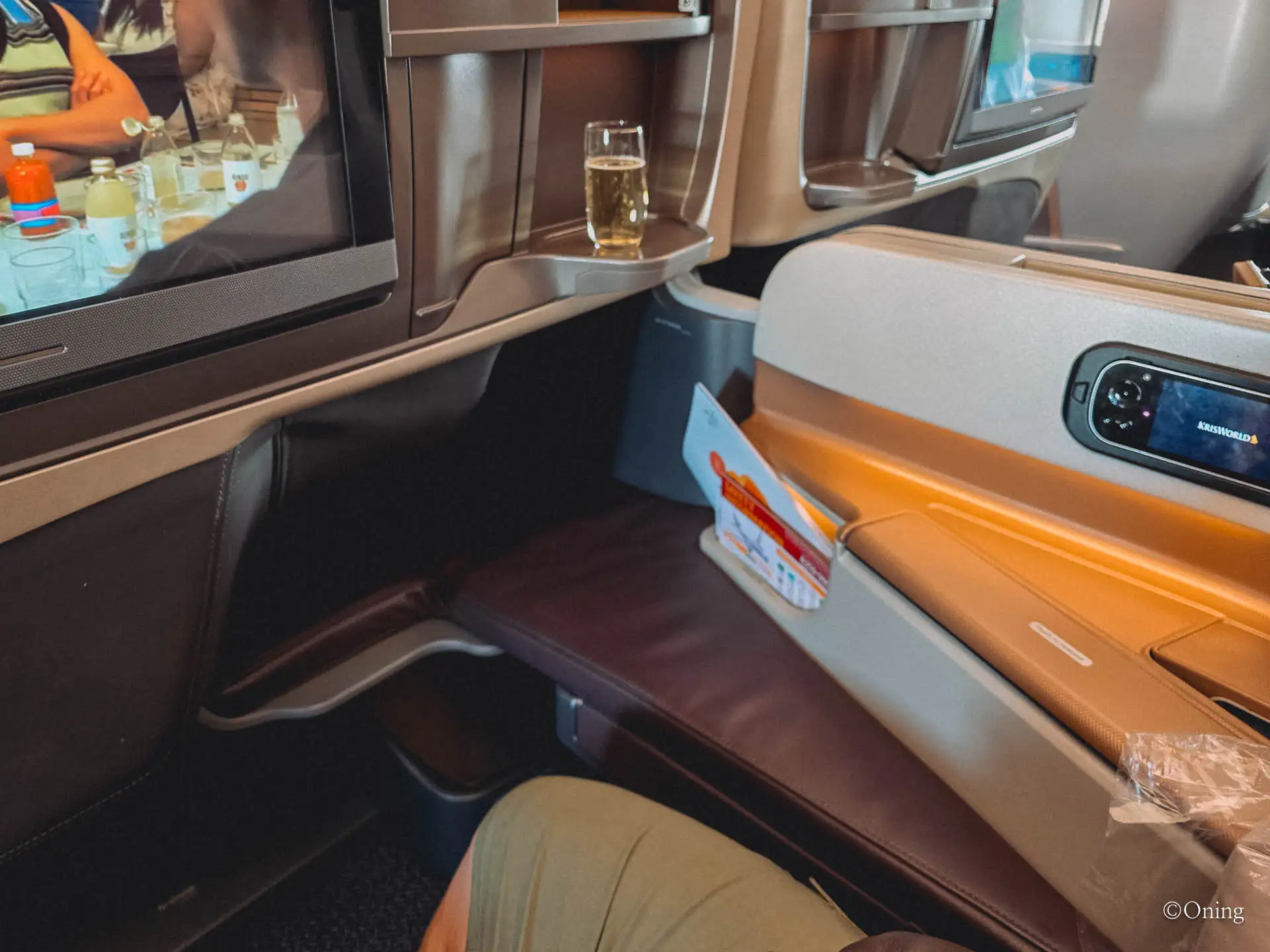 A Singapore Airlines business class seat reclined into its angled lie-flat position with the ottoman offset diagonally, beside a welcome glass of champagne — not a true full-flat seat