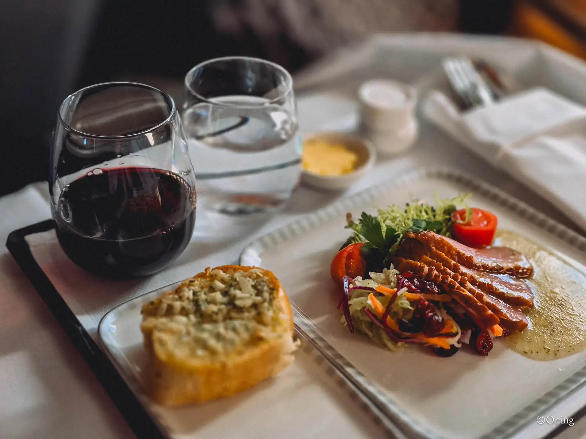 Business class meal tray with red wine, garlic bread and a smoked duck salad starter
