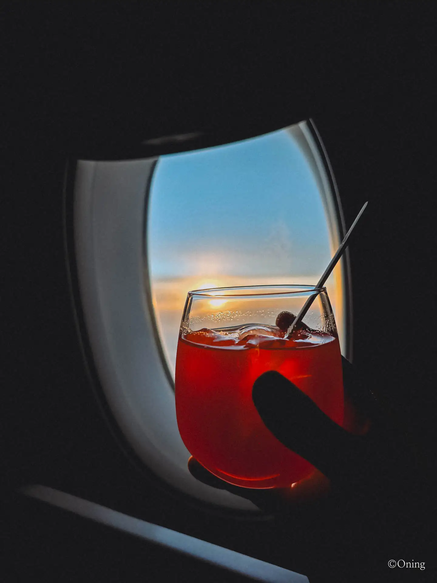 A Singapore Sling cocktail held against the cabin window at sunset