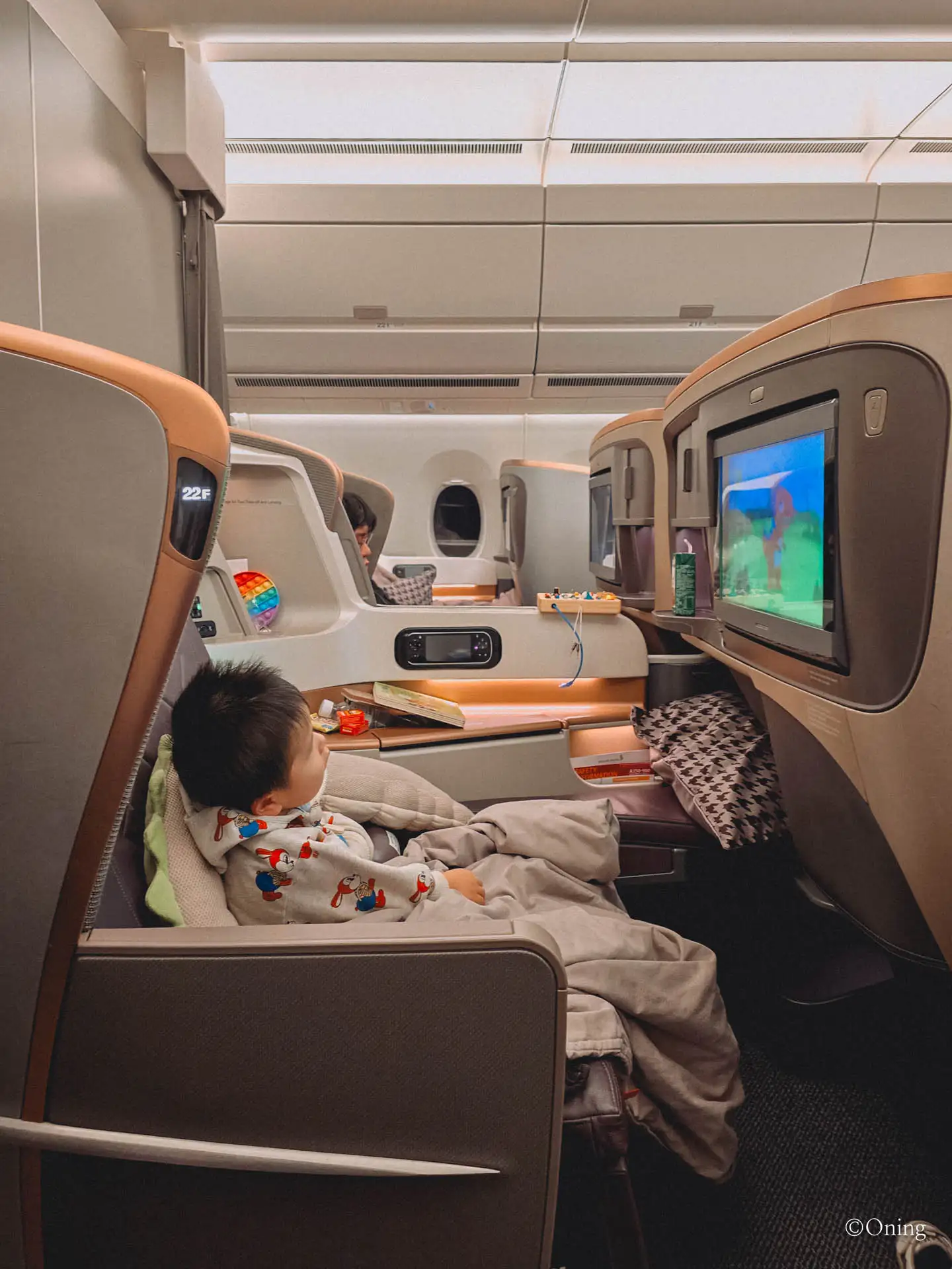 A toddler watching in-flight entertainment from a reclined business class seat