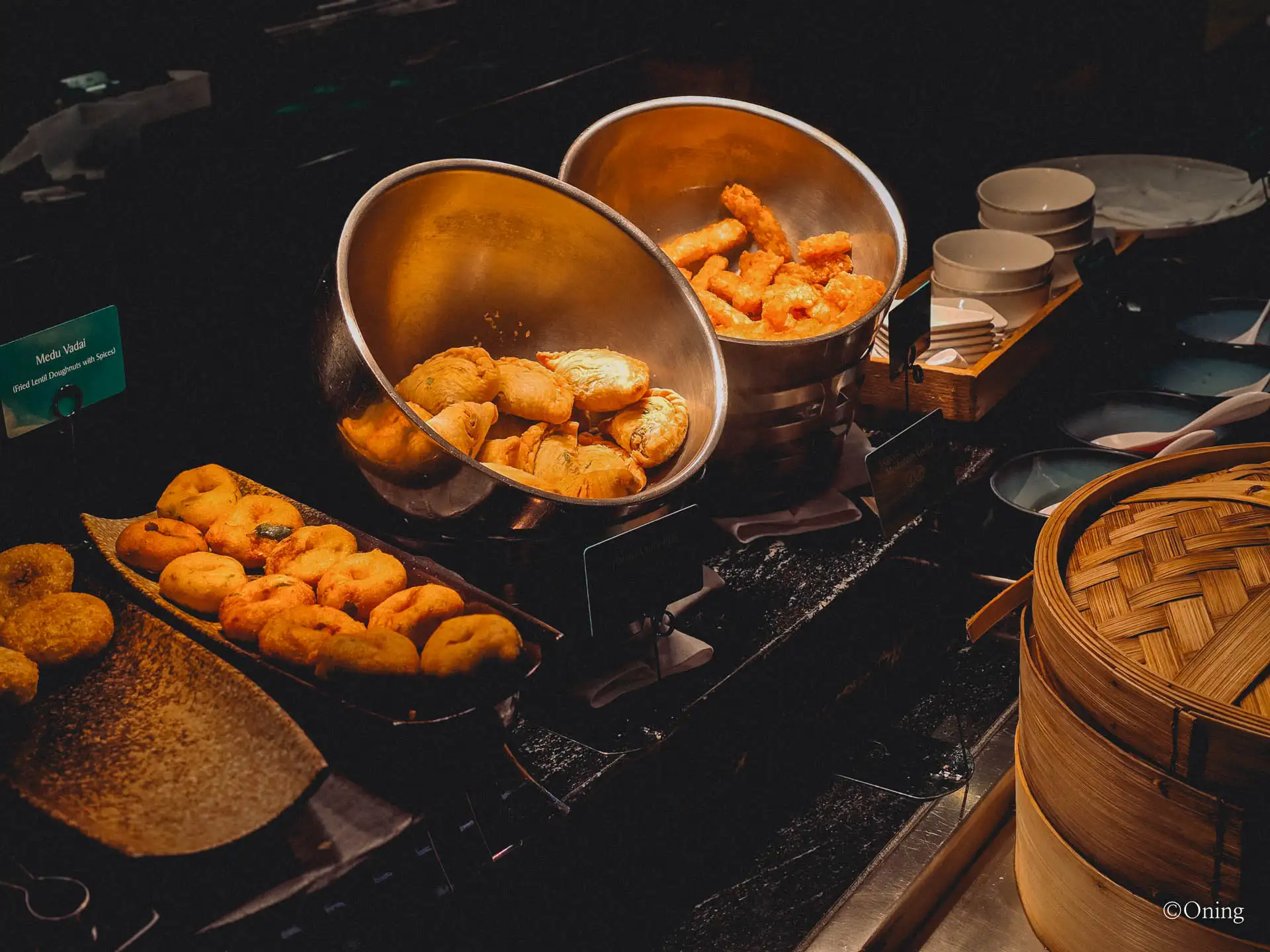 Fried snacks including medu vadai and samosas with bamboo steamers at the lounge