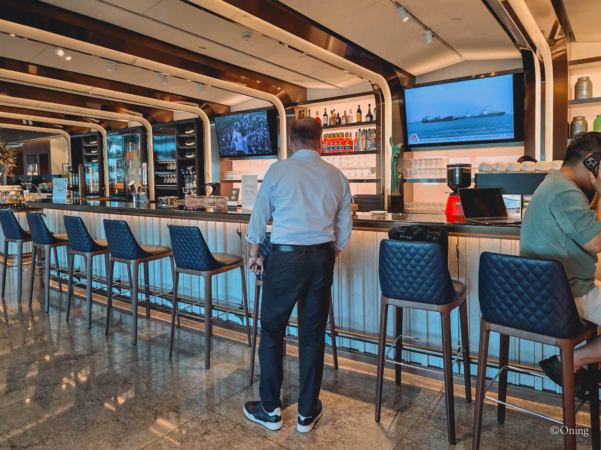 A bar with staff and TV screens in the quieter area of the SilverKris Lounge